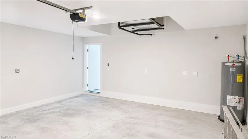 Spacious garage featuring concrete flooring, a ceiling-mounted garage door opener, and a water heater