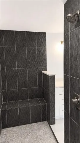 Walk-in shower featuring textured dark gray wall tiling, a built-in tiled bench, and pebble-finish floor tiling