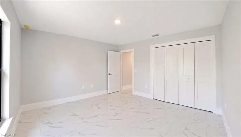 Spacious room featuring large format tile flooring, light gray wall color, white baseboards, and bi-fold closet doors