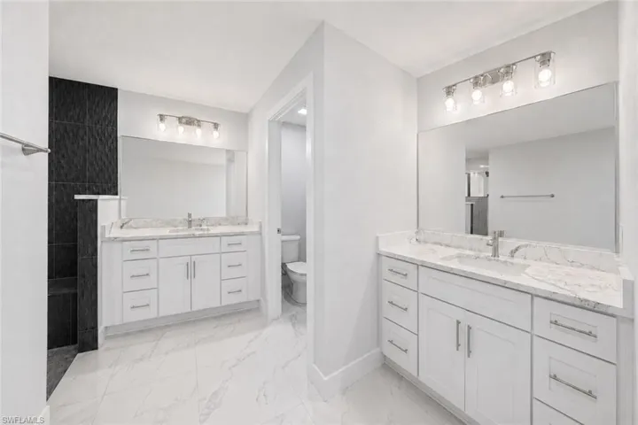 Dual vanity bathroom featuring white cabinetry, light-toned countertops, and large format floor tiling