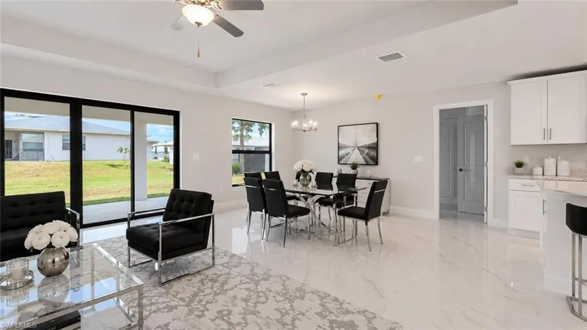 Open-concept living space featuring high ceilings, large format tile flooring, a contemporary dining area with a chandelier, and expansive sliding glass doors leading to the exterior