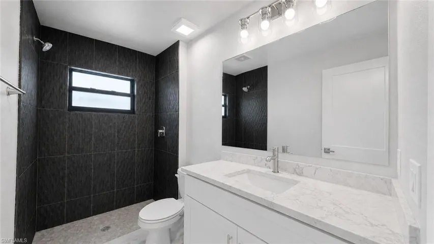 Contemporary bathroom featuring a spacious vanity with a white countertop and undermount sink, a large wall mirror, and a walk-in shower with dark textured tile walls and a window