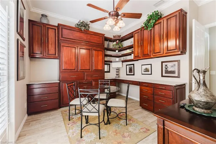 Bedroom with Murphy bed folded up featuring built in office/study area, ceiling fan, ornamental molding, light wood finished floors, and light stone countertops