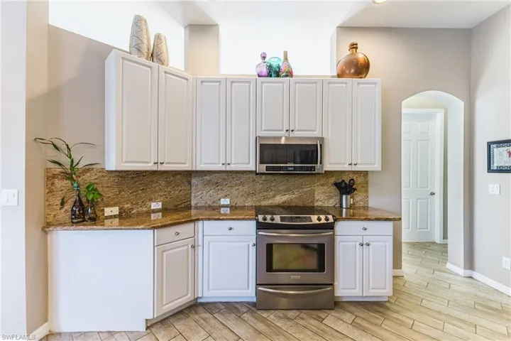 Kitchen featuring stainless steel appliances, dark stone counters, white cabinetry, and wood tiled floors