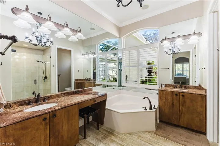 Bathroom with a chandelier, a stall shower, two vanities, a bath, and ornamental molding