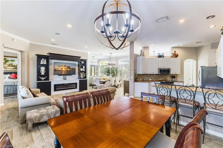 Dining space with arched walkways, a glass covered fireplace, light wood-style flooring, recessed lighting, and ornamental molding