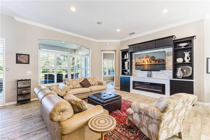Living area featuring a glass covered fireplace, crown molding, light wood-style flooring, and recessed lighting