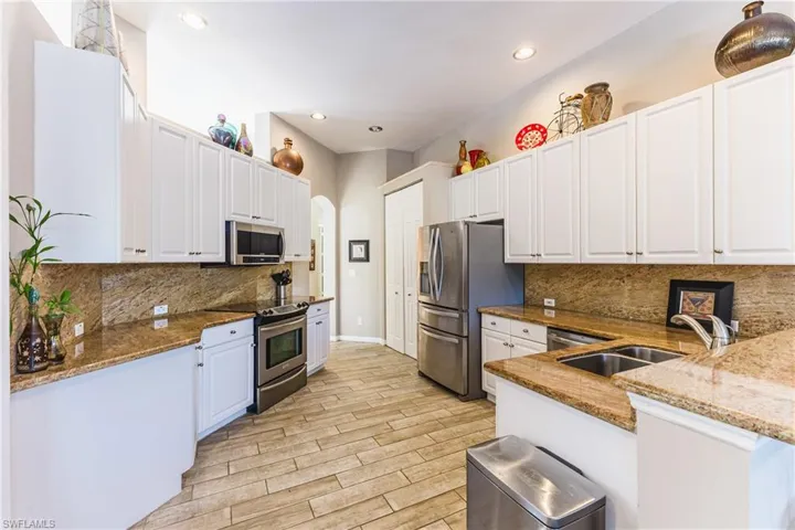 Kitchen featuring white cabinetry, stainless steel appliances, wood tiled floors, dark stone counters, and recessed lighting