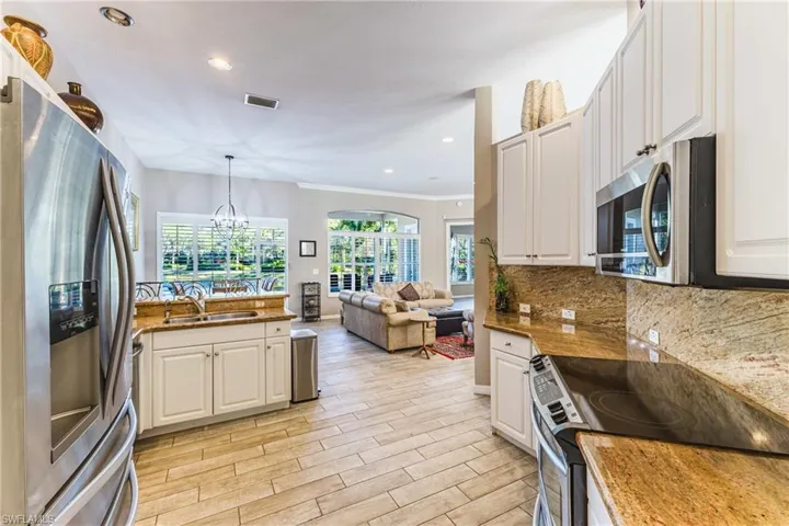 Kitchen with stainless steel appliances, open floor plan, wood finish floors, white cabinets, and ornamental molding