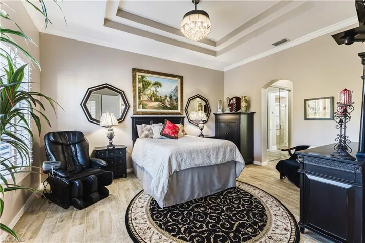 Bedroom featuring crown molding, light wood-style flooring, arched walkways, a chandelier, and a tray ceiling