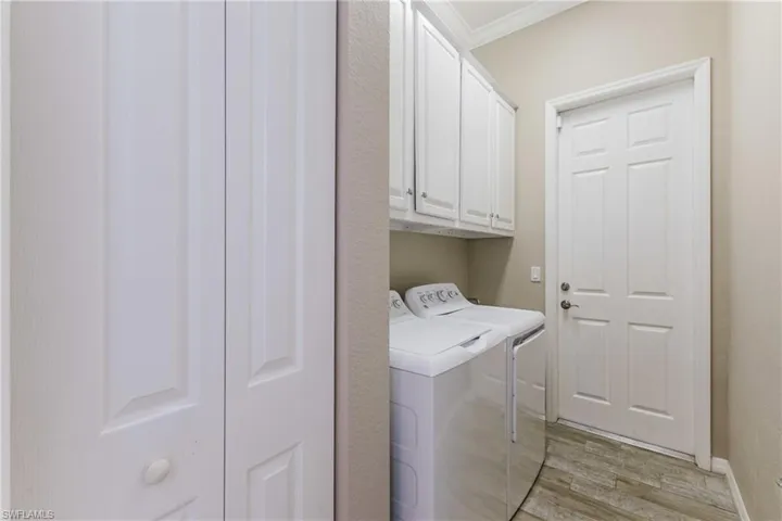 Laundry area featuring light wood-type flooring, cabinet space, crown molding, and washing machine and clothes dryer