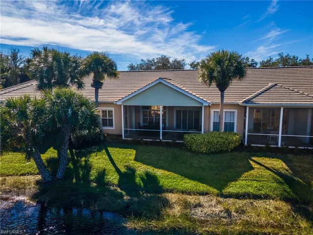 Rear view of house with a screened lanai, a tile roof, a lawn, and a water view with fountain
