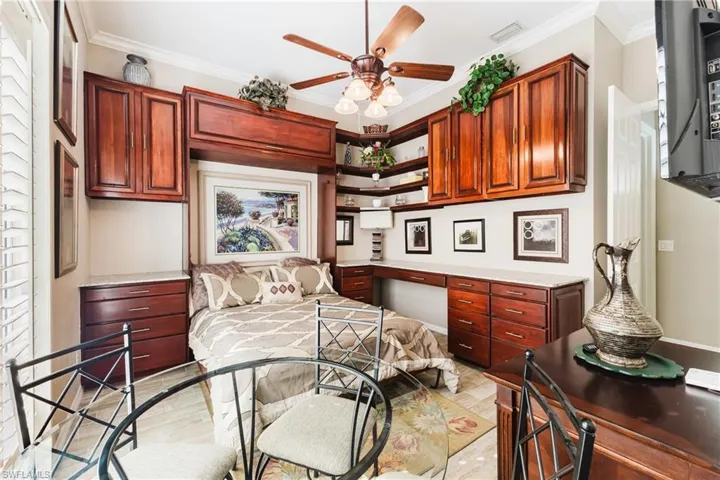 Bedroom with built in desk, Murphy bed, light wood-style floors, ornamental molding, and a ceiling fan