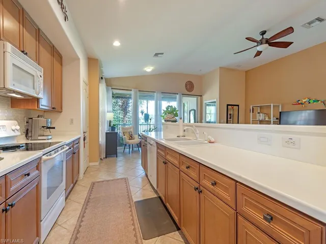 Kitchen featuring coastal white appliances, lots of counterspace, cabinetry and a lofted ceiling, which opens to the living/dining areas of the home.