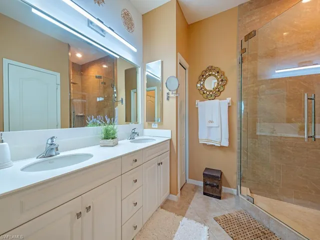 Primary Bathroom with walk-in shower, light tile patterned tile floors, high ceilings and double vanity