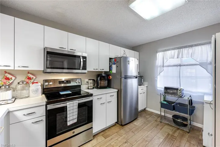 Kitchen featuring stainless steel appliances, light countertops, white cabinets, a textured ceiling, and light wood-style flooring