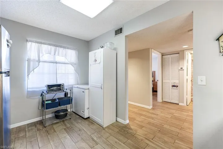 Kitchen featuring a textured ceiling, light wood finished floors, white fridge, freestanding refrigerator, and white cabinetry
