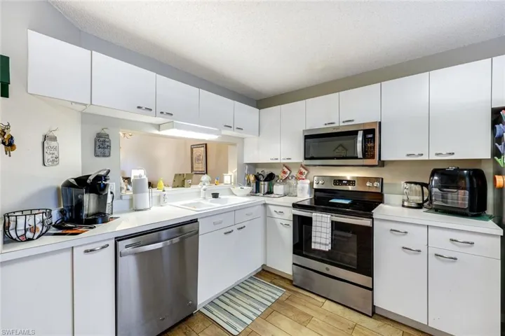 Kitchen featuring stainless steel appliances, light countertops, white cabinetry, a textured ceiling, and light wood-style flooring