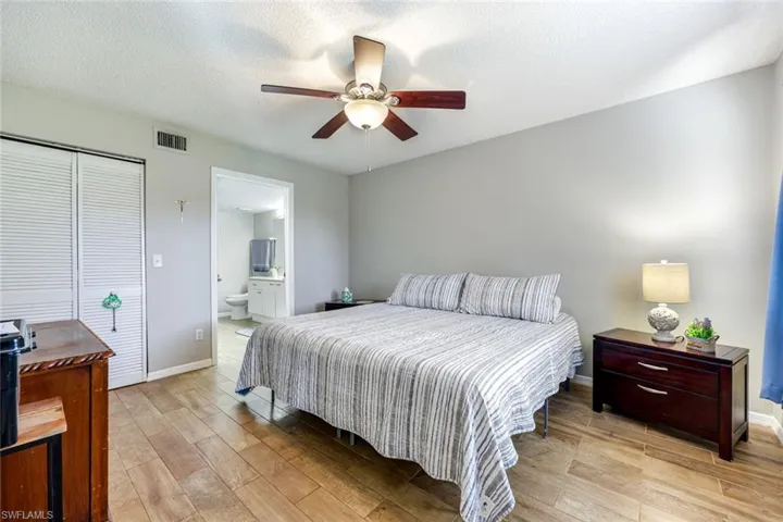 Bedroom with light wood-type flooring, ceiling fan, ensuite bathroom, a textured ceiling, and a closet