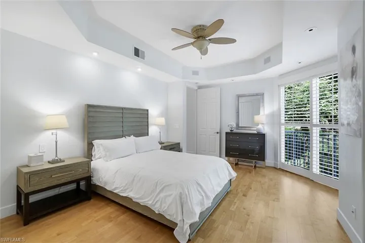 Bedroom with a tray ceiling, light wood-style floors, ceiling fan, and recessed lighting