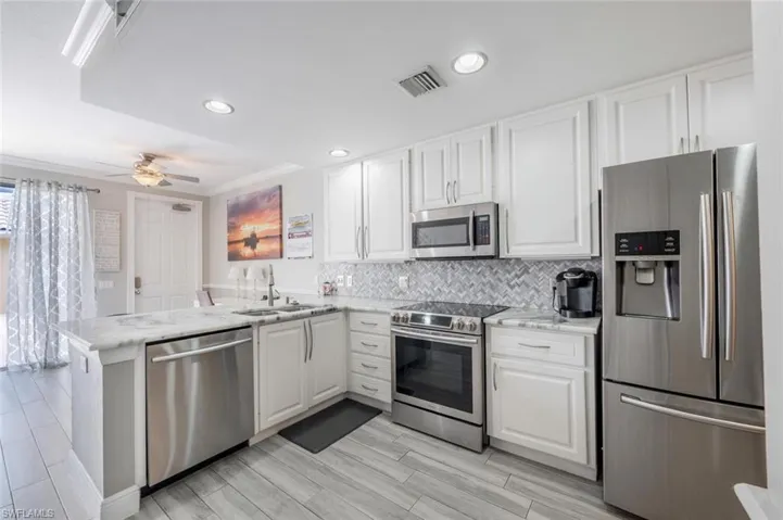 Kitchen with ceiling fan, stainless steel appliances, white cabinets, sink, and kitchen peninsula