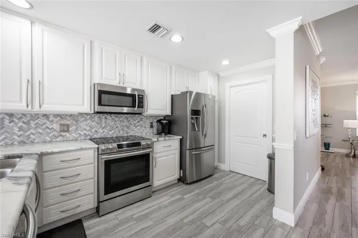 Kitchen featuring light hardwood / wood-style flooring, stainless steel appliances, white cabinets, decorative backsplash, and ornamental molding