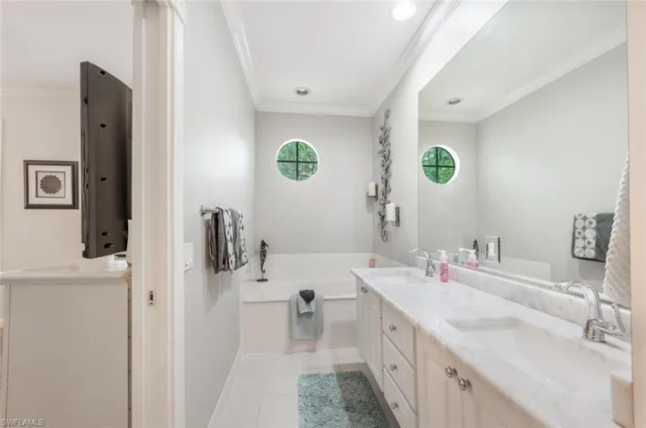 Bathroom with tile patterned flooring, double sink vanity, crown molding, and a bath