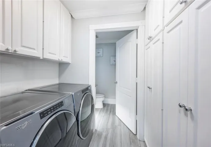 Laundry area featuring washing machine and dryer, light hardwood / wood-style flooring, cabinets, and ornamental molding