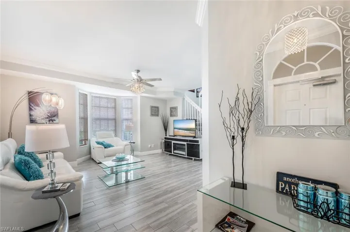 Living room with ceiling fan with notable chandelier, crown molding, and light wood-type flooring