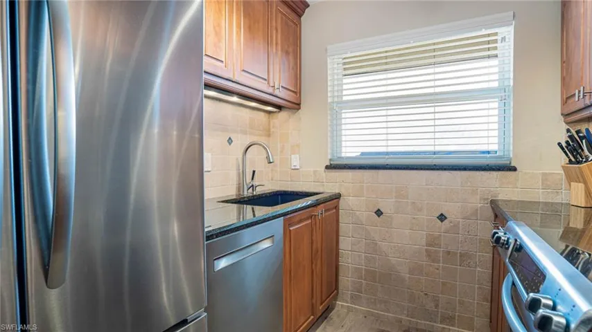 Kitchen with stainless steel appliances, dark stone counters, tile walls, a healthy amount of sunlight, and sink
