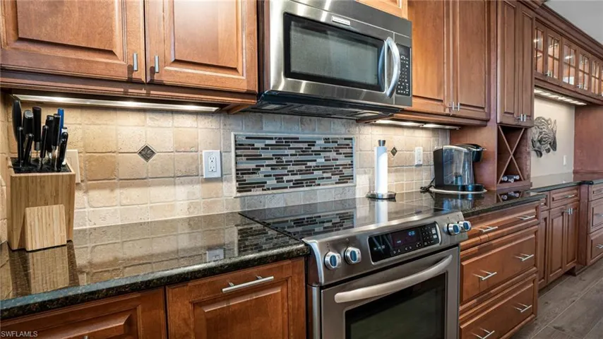 Kitchen with stainless steel appliances, dark stone countertops, wood-type flooring, and decorative backsplash