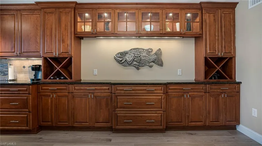 Bar with wood-type flooring, decorative backsplash, and dark stone countertops