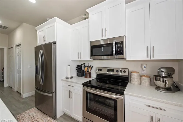 Kitchen with appliances with stainless steel finishes, white cabinetry, light stone countertops, wood finish floors, and recessed lighting