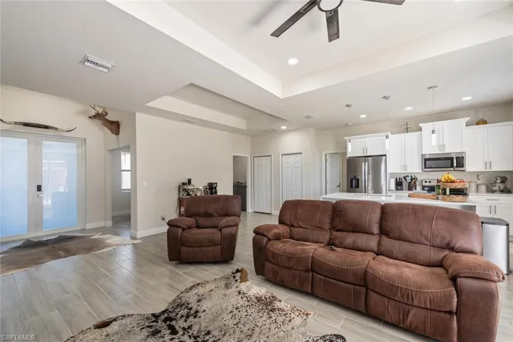 Living room with a tray ceiling, wood tiled floors, french doors, and ceiling fan