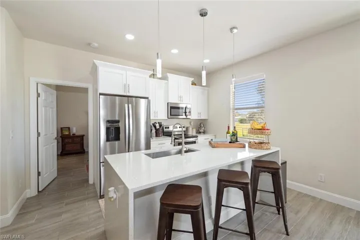 Kitchen with light stone counters, a kitchen bar, appliances with stainless steel finishes, hanging light fixtures, and recessed lighting