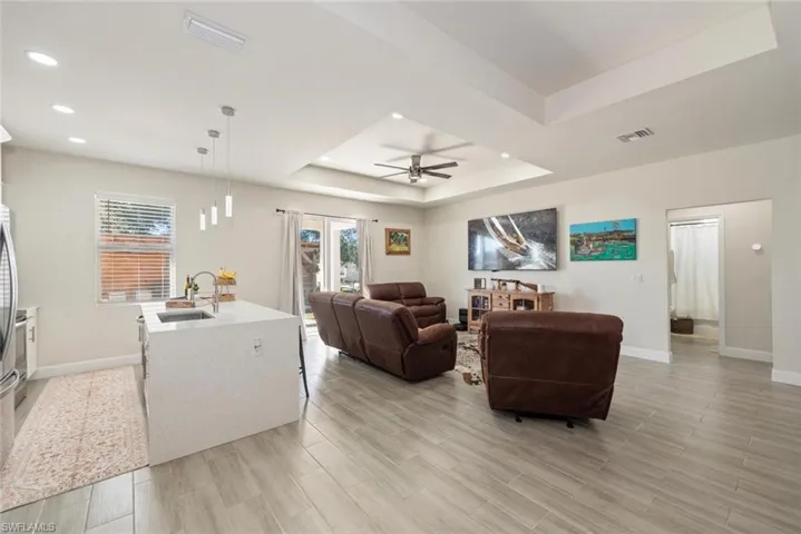 Living room featuring a raised ceiling, wood tiled floors, a ceiling fan, and recessed lighting
