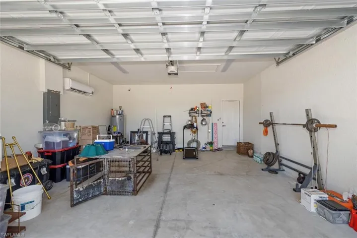Garage featuring electric panel, a wall unit AC, and water heater