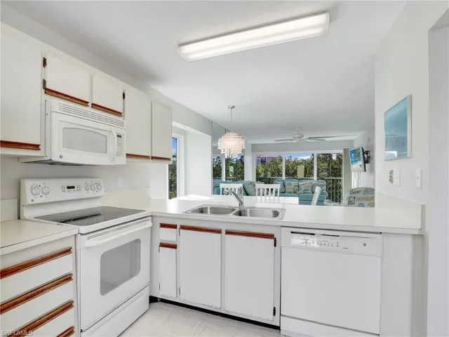 Kitchen featuring white appliances, sink, decorative light fixtures, white cabinetry, and plenty of natural light
