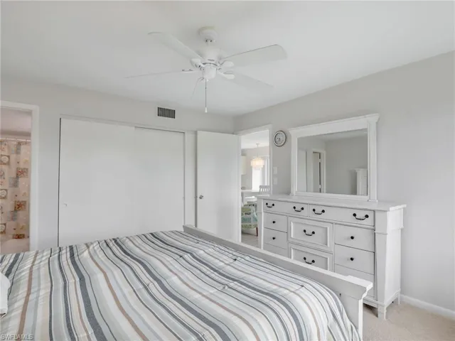 Bedroom with a closet, light colored carpet, ensuite bath, and ceiling fan