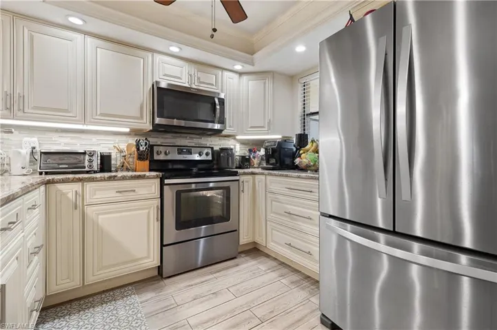 Kitchen with ornamental molding, stainless steel appliances, ceiling fan, wood finish floors, and light stone countertops