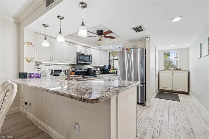 Kitchen featuring a peninsula, dark stone counters, stainless steel appliances, light wood-style flooring, and decorative light fixtures