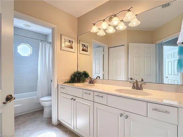 Bathroom with double vanity, shower / tub combo, and light tile patterned floors