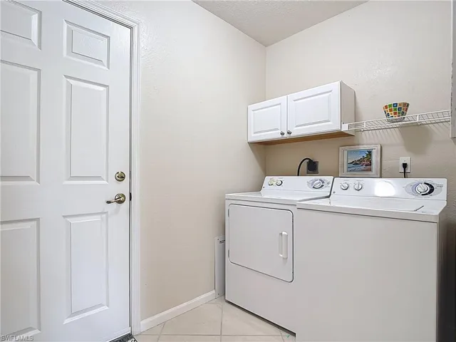 Laundry room featuring light tile patterned floors, independent washer and dryer, a textured ceiling, and cabinet space