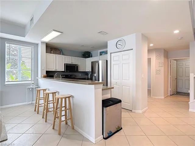 Kitchen with white cabinets, appliances with stainless steel finishes, a breakfast bar, light tile patterned flooring, and a peninsula