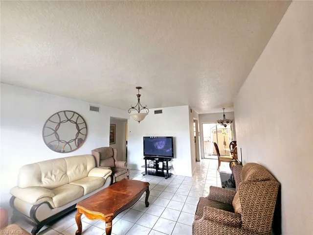 Living room with a textured ceiling, a notable chandelier, and light tile patterned floors