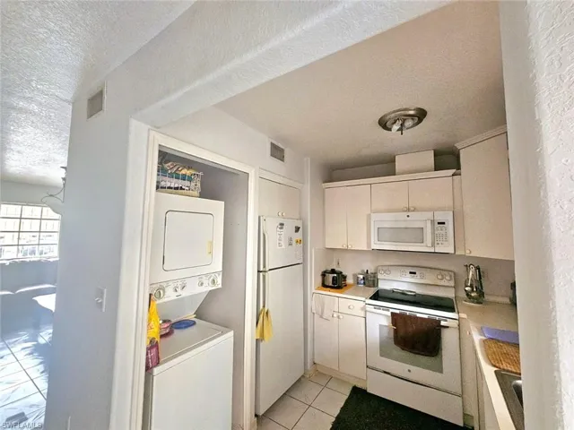 Kitchen featuring stacked washer and clothes dryer, a textured ceiling, light tile patterned floors, and white appliances
