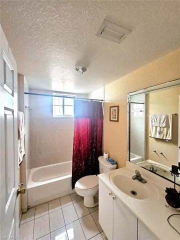 Full bathroom with shower / tub combo with curtain, vanity, toilet, a textured ceiling, and tile patterned flooring