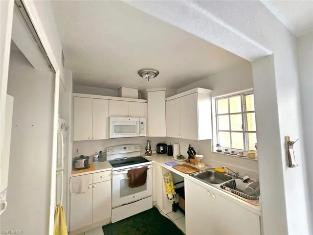 Kitchen featuring white appliances, sink, light tile patterned floors, a textured ceiling, and white cabinetry