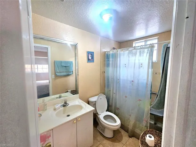 Bathroom with tile patterned flooring, toilet, vanity, and a textured ceiling