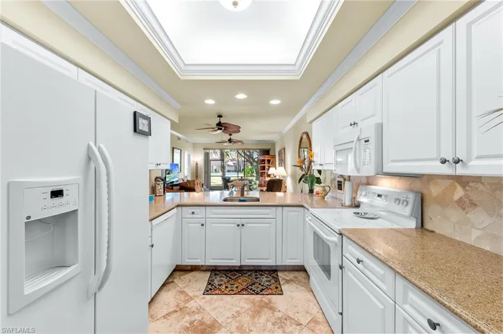 Kitchen featuring white appliances, open floor plan, white cabinetry, crown molding, and light stone countertops